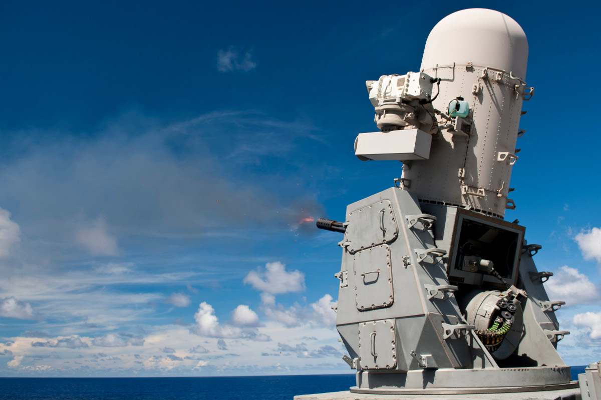 A Phalanx close-in weapons system (CIWS) aboard the Ticonderoga-class guided-missile cruiser USS Cowpens (CG 63) fires at a missile decoy towed by a jet on a long cable.